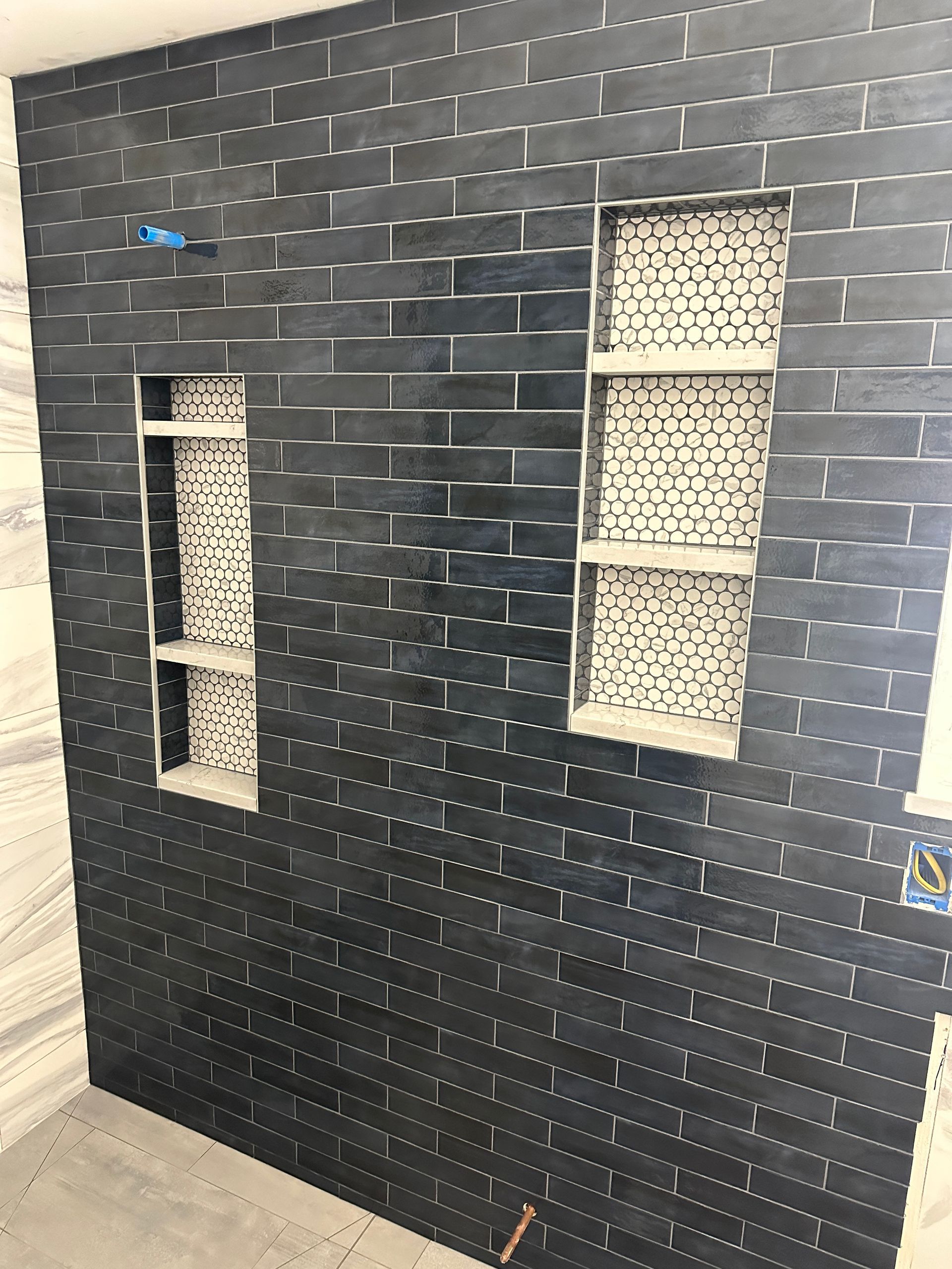 A black brick wall with two shelves in it in a bathroom.