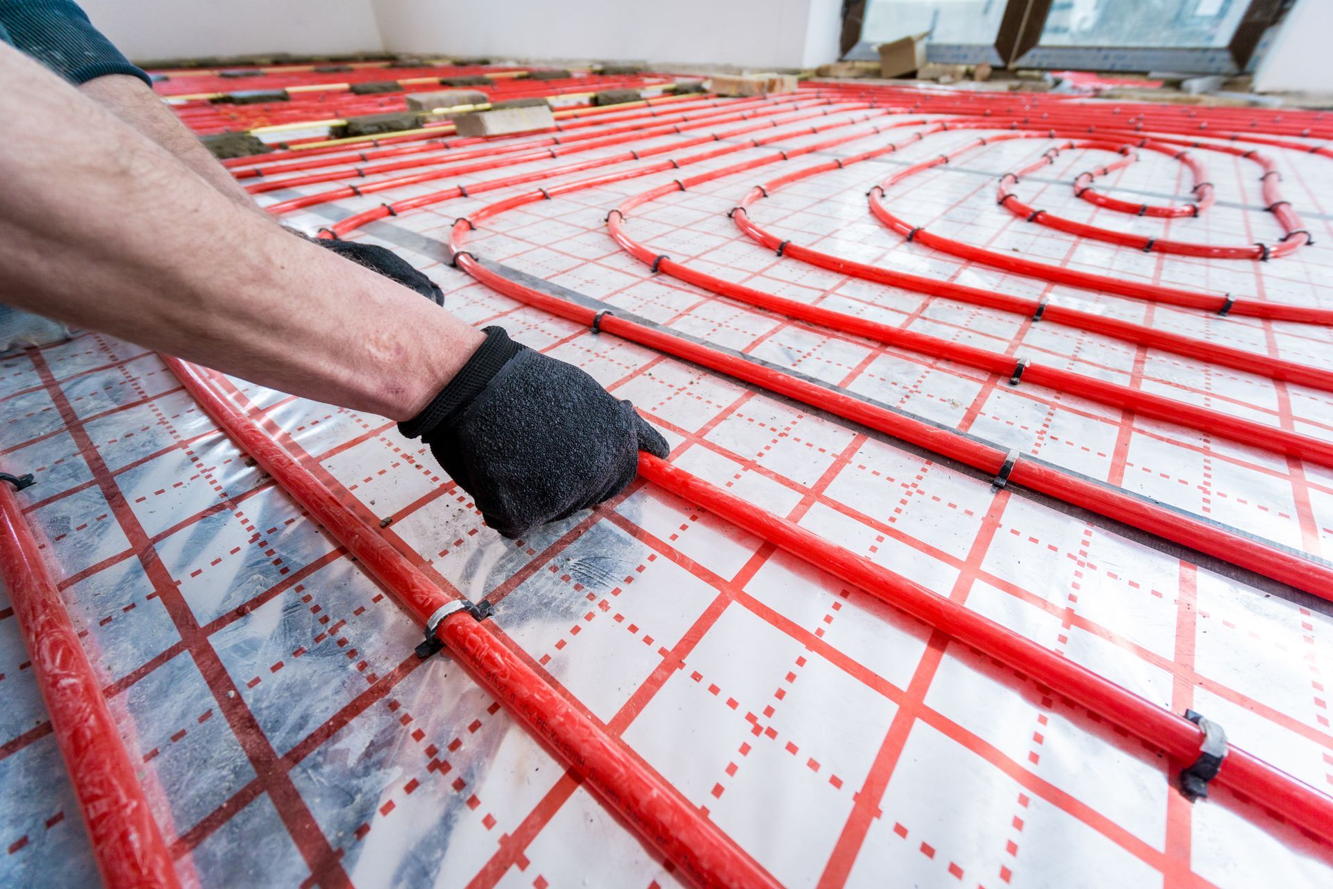 Person installing radiant floor heating tubes on a grid. Red tubes on a silver surface.