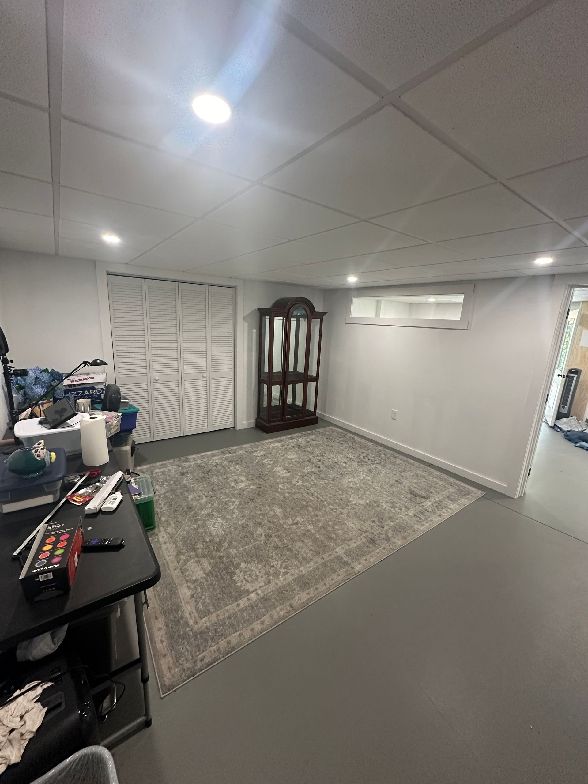 A living room in a basement with a rug and a hutch.