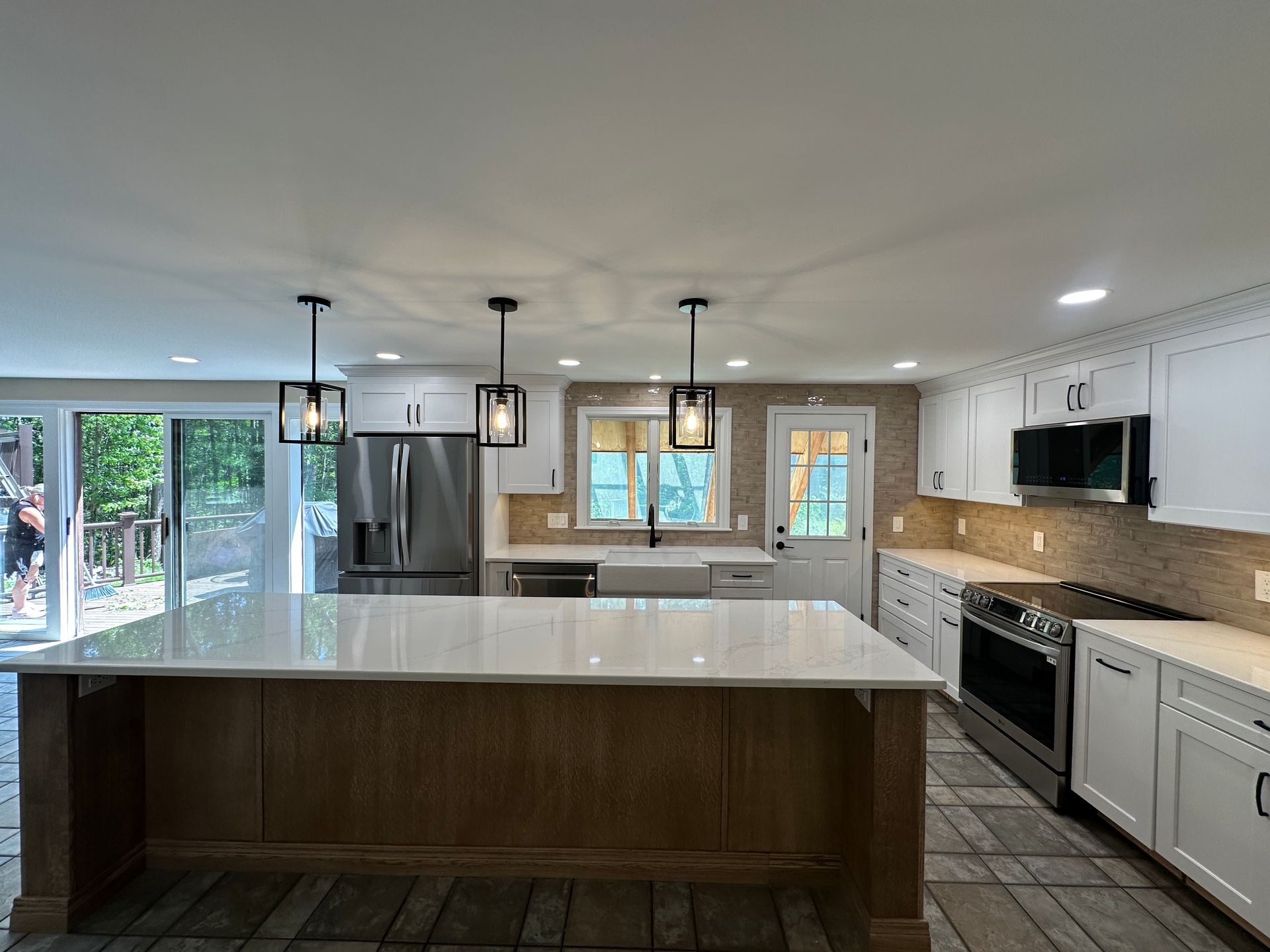 Modern kitchen with large island, pendant lights, stainless appliances, white cabinets, and tile floor.