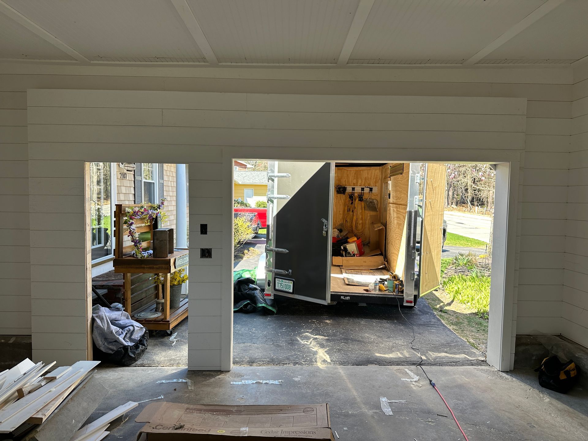 A garage with an open bay door, showing a trailer outside and household items inside.