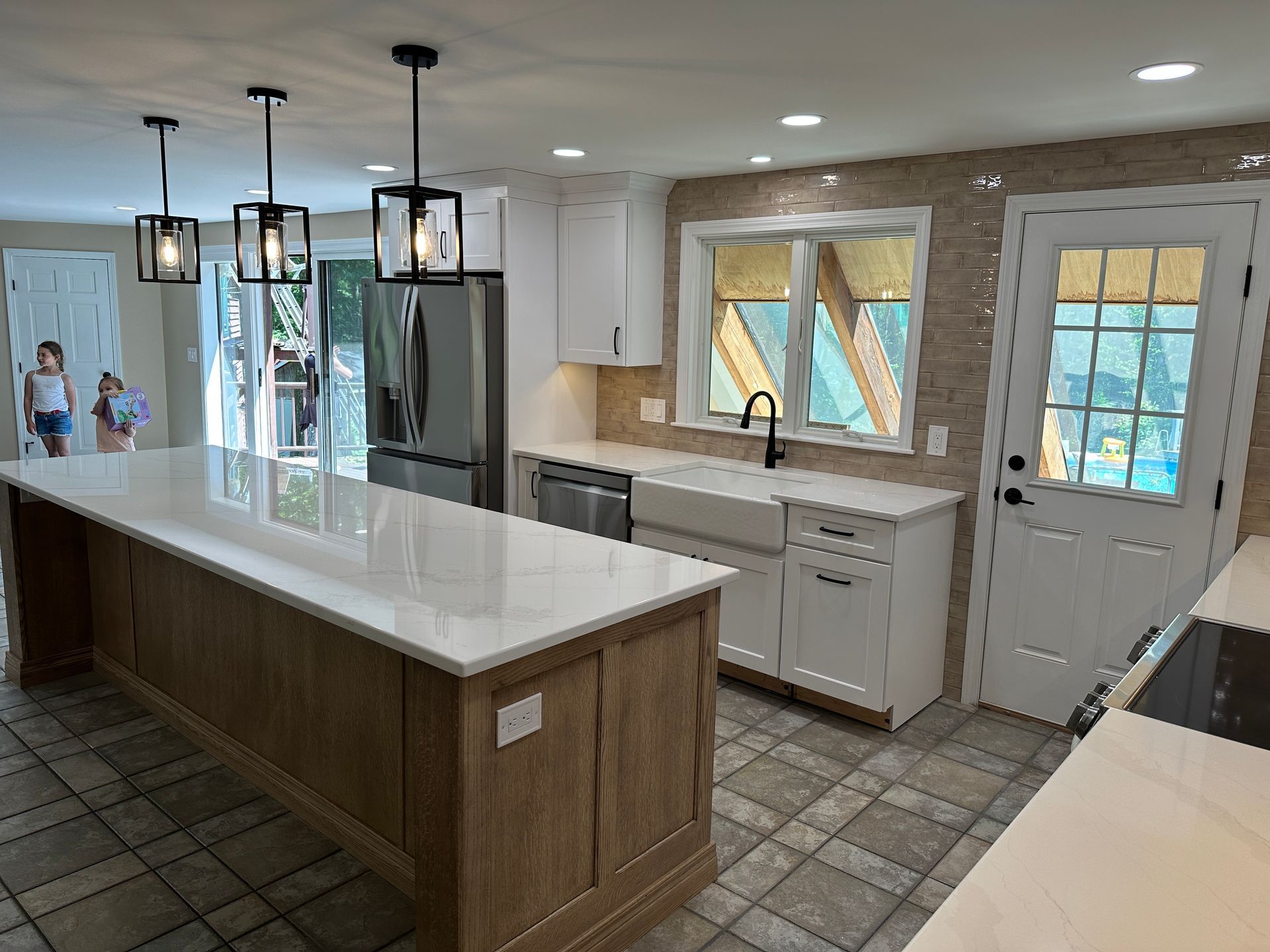 A kitchen with a large island , white cabinets , stainless steel appliances , and a refrigerator.