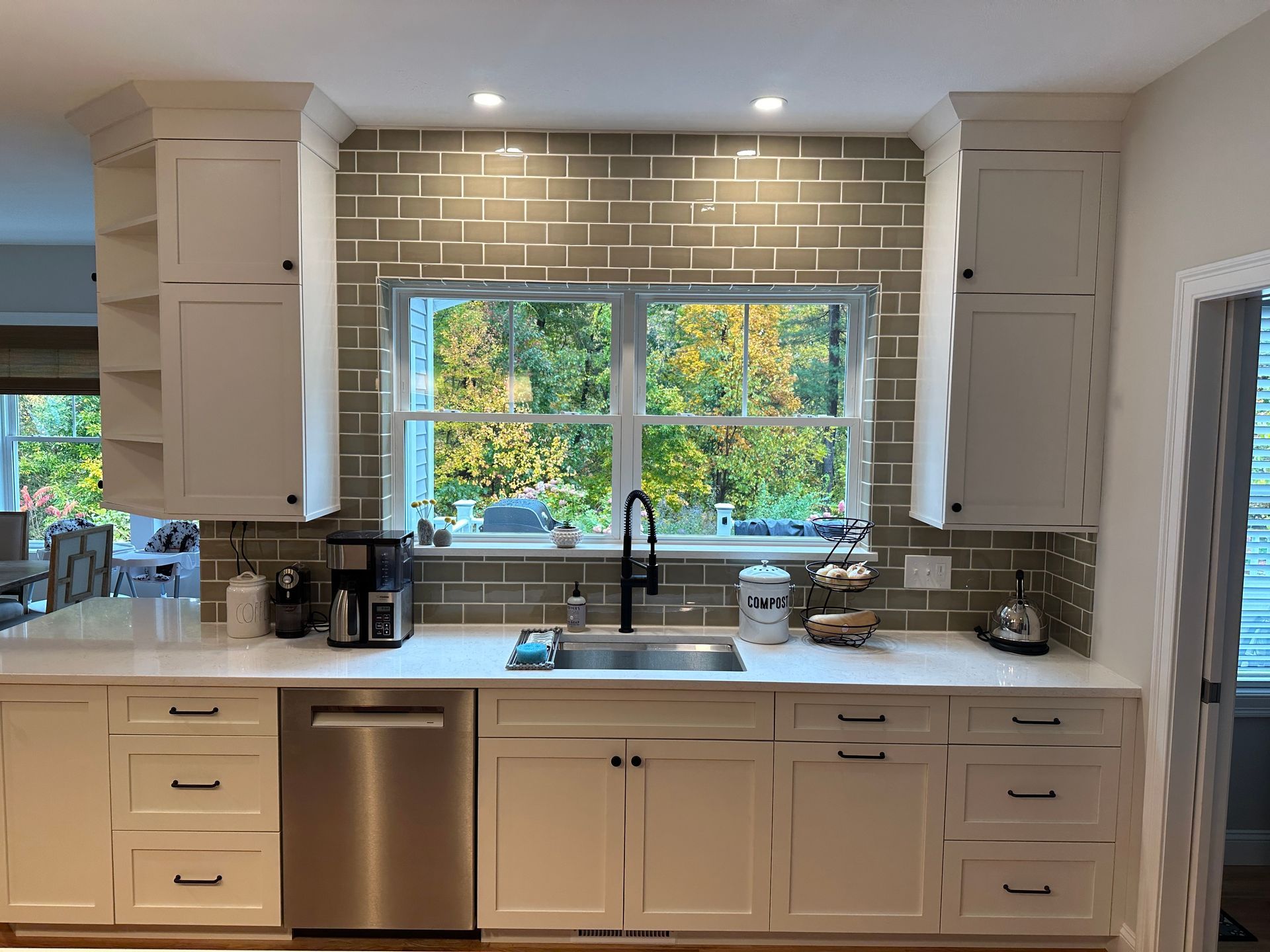 Modern kitchen with white cabinets, stainless dishwasher, brick backsplash, and a window over the sink.