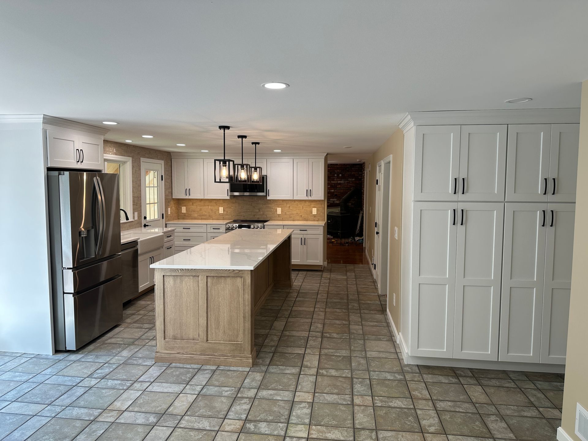 Spacious kitchen with a light-colored island and cabinets. Stainless steel appliances and stone tile flooring.