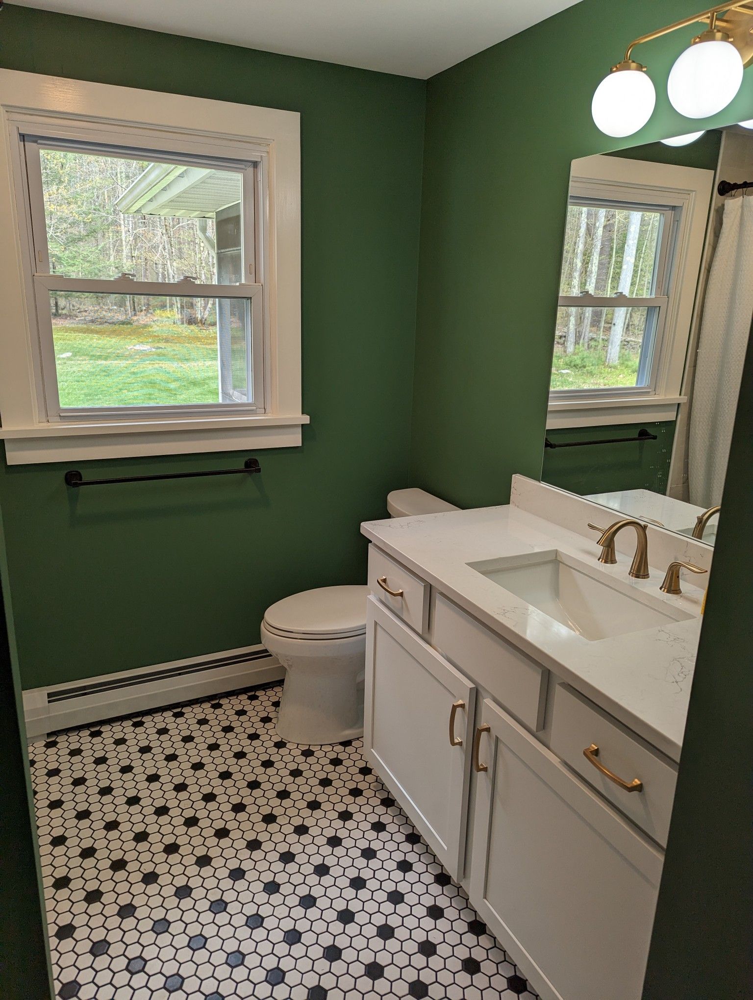 A bathroom with green walls , white cabinets , a toilet , sink and mirror.