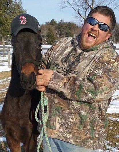 photo of man with his Hackney Pony; pony is wearing a Red Sox baseball hat