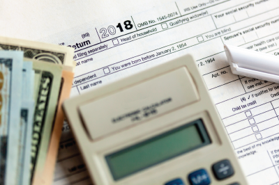 Tax forms, money, and calculator on a desk. Focus on the 2018 tax year form.