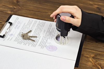 Hand stamping a document with a seal, keys on the paper; wooden table background.