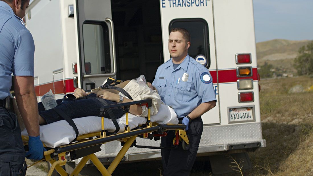 Two EMTs carrying a patient on a stretcher toward an ambulance.
