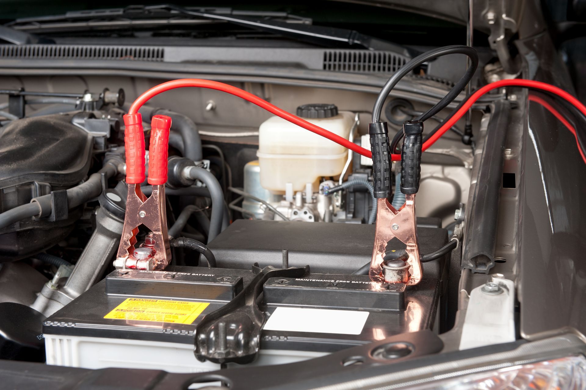 Car battery being jump-started with red jumper cables, set in a vehicle's engine bay.