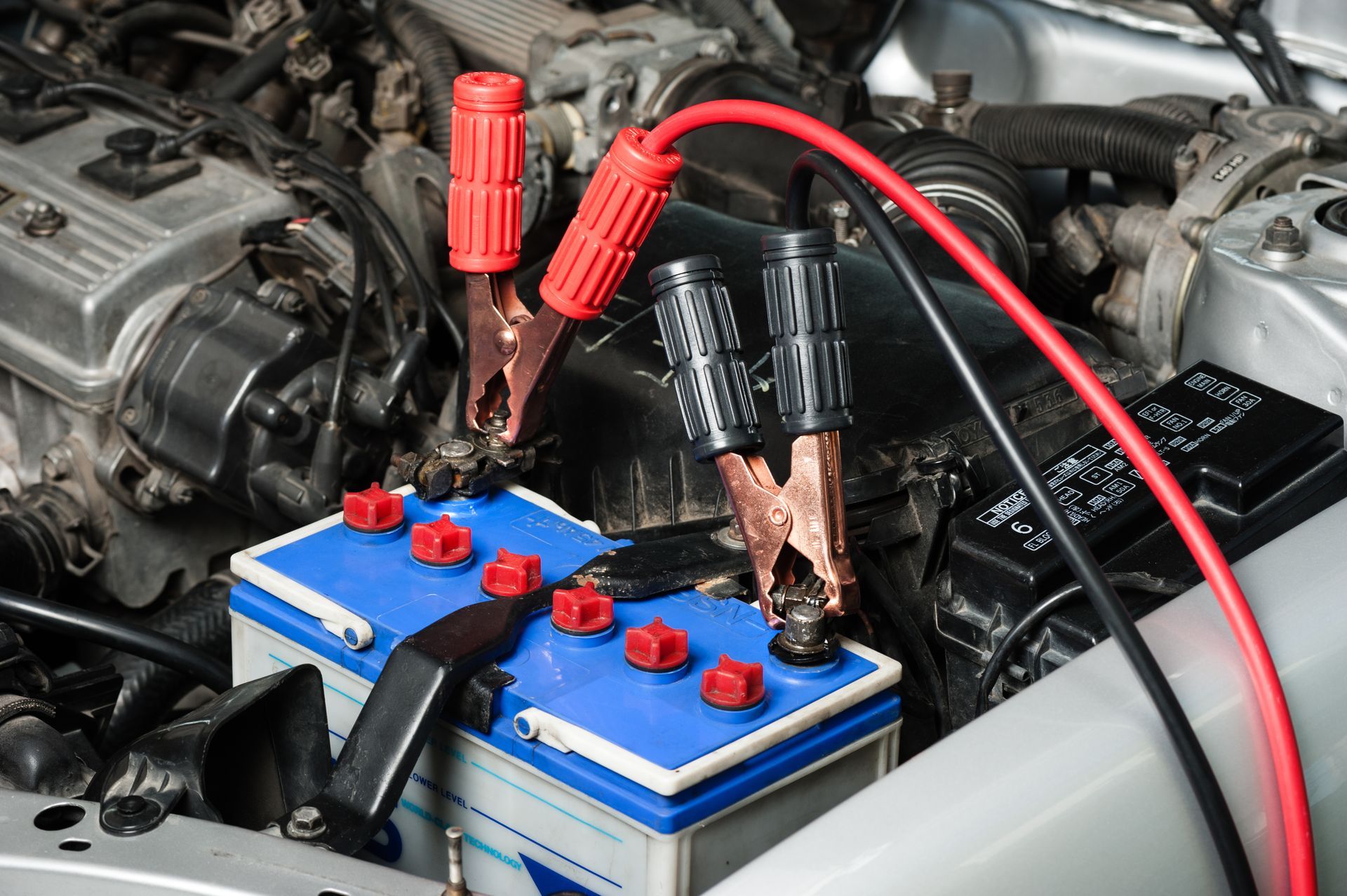 Car battery being jump-started with red and black cables attached, in a vehicle's engine bay.