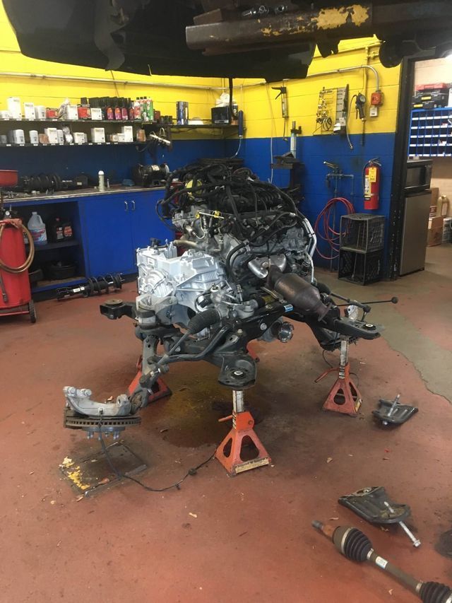 Engine and suspension on jack stands in a car repair shop. Red and yellow interior with tools and equipment.