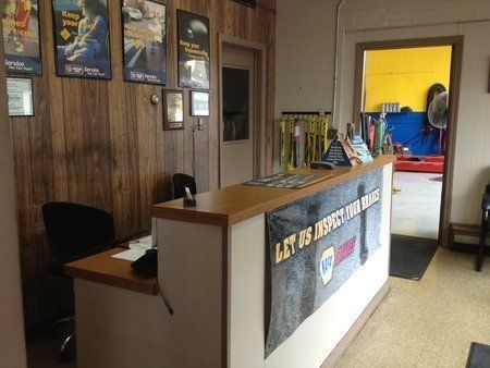 Reception area of an auto repair shop with a desk, wood paneling, and a view into the garage.