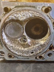 Close-up of a heavily corroded engine cylinder head with two valves, showing significant wear and damage.