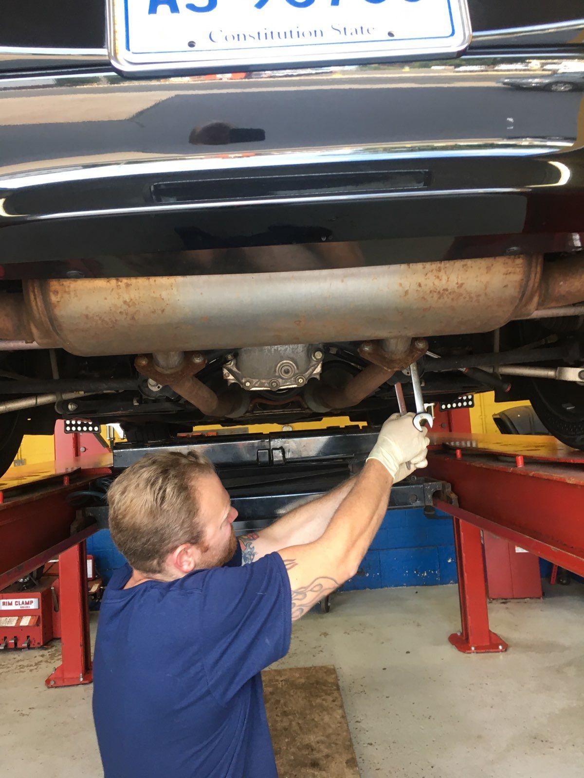 Mechanic working under a car, using a wrench. Located in a garage with red lifts.
