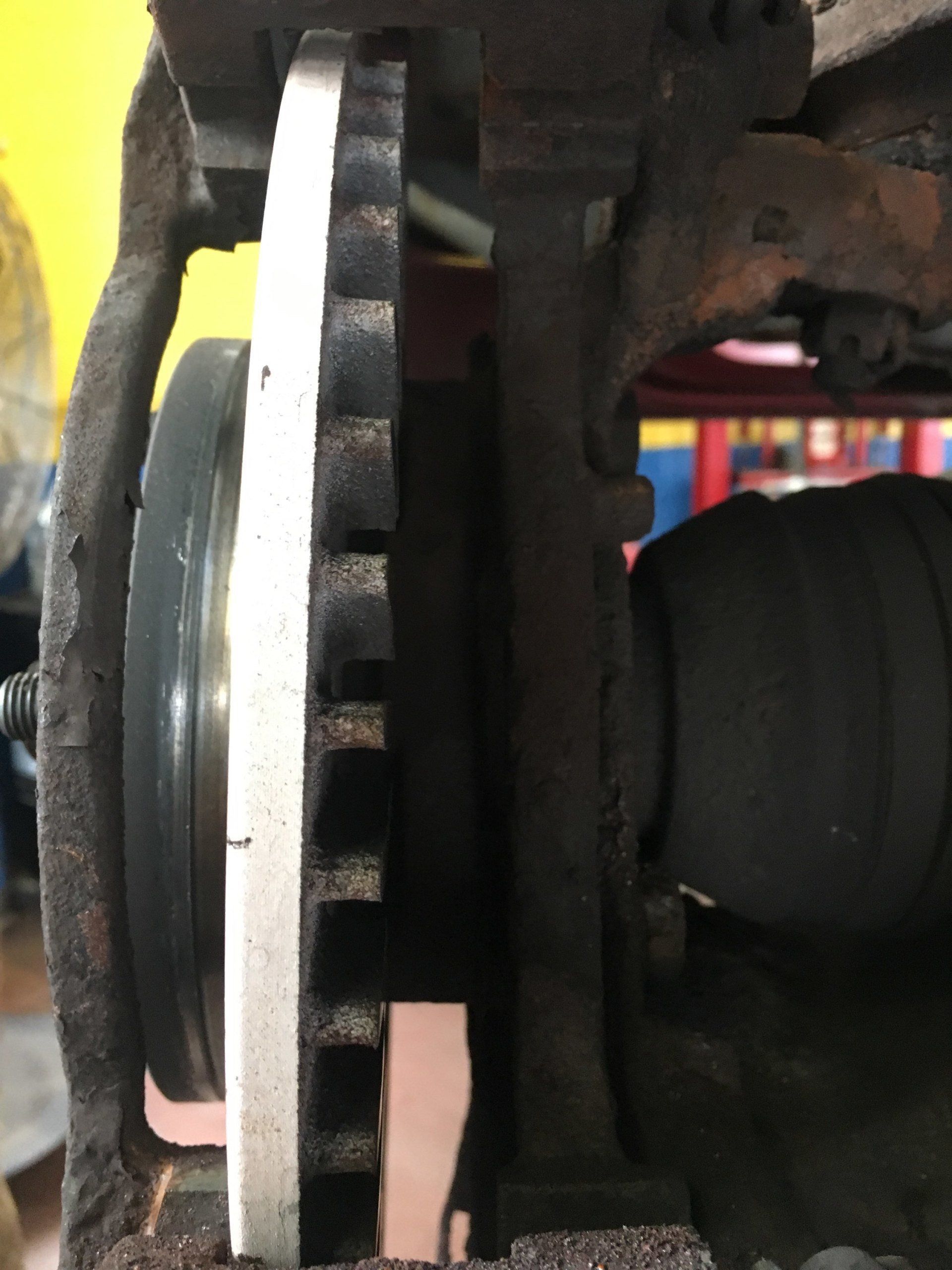 Close-up of a car brake rotor. A new silver rotor sits between a caliper and hub, illustrating the new brake assembly.