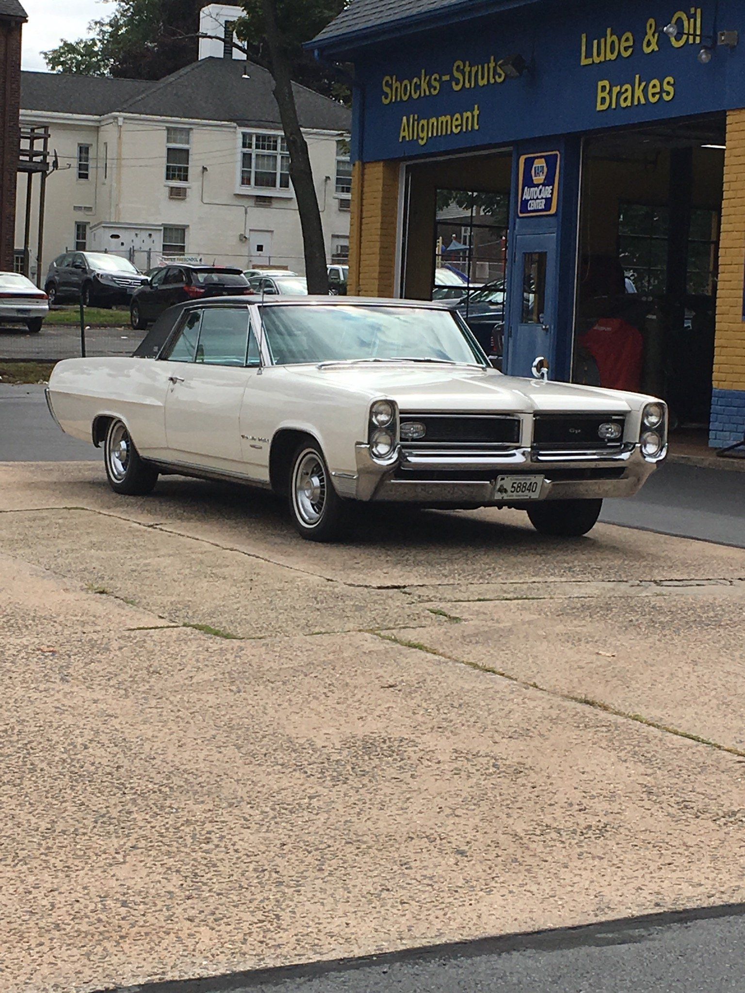 White classic car parked in front of a car repair shop.