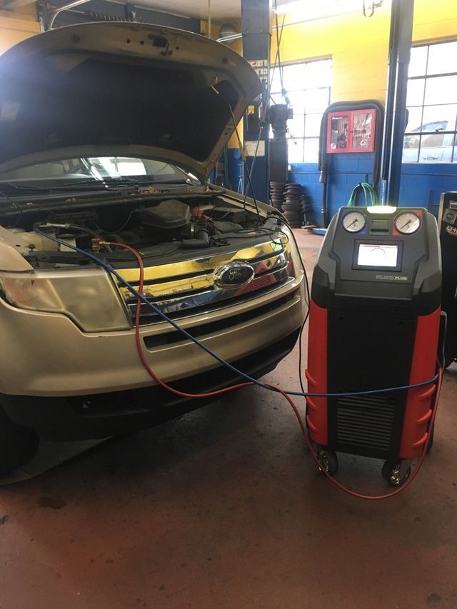 A car at a shop being serviced for AC. Hoses connect the car to a large red and black machine.