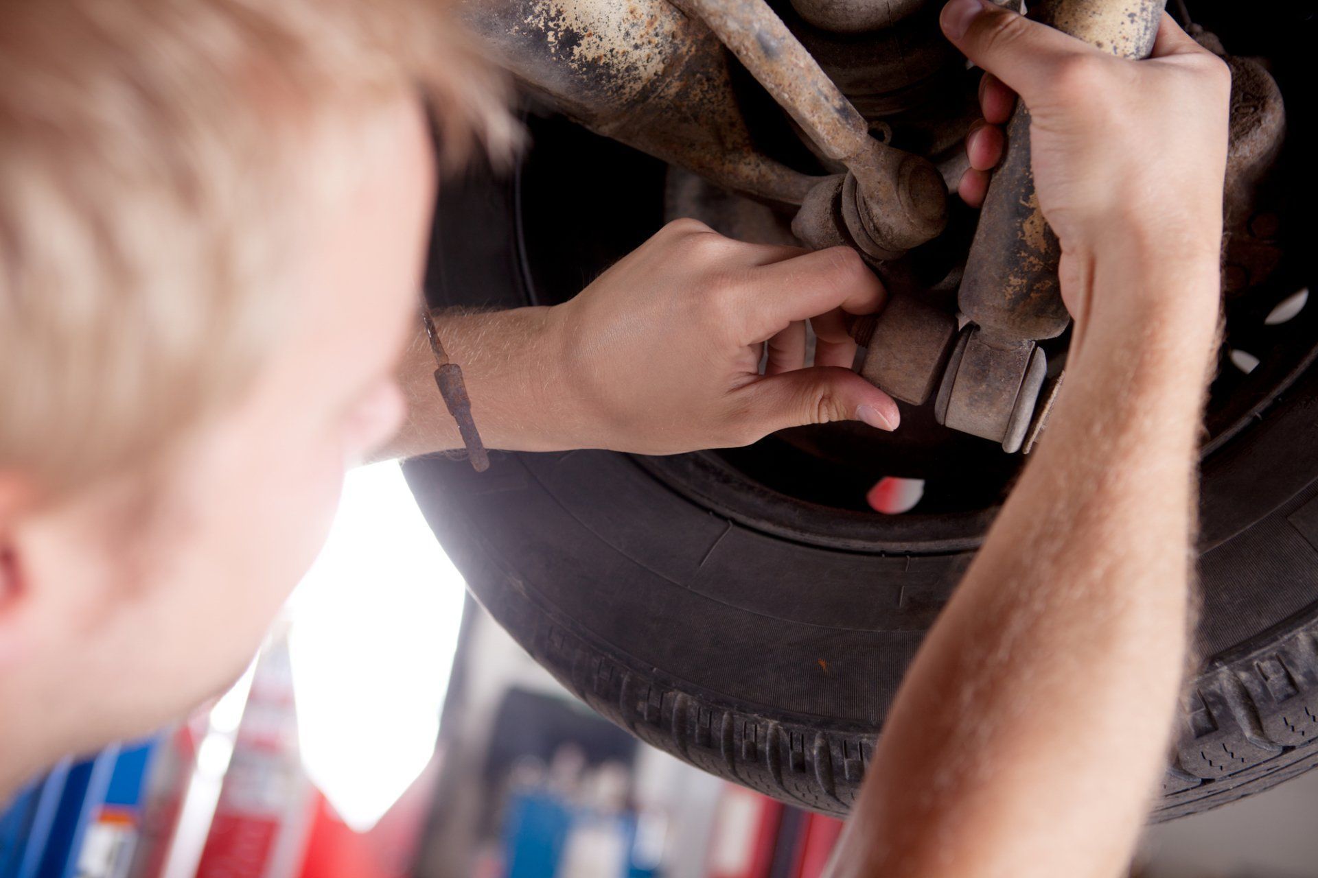 Mechanic works on a car's suspension, inspecting a part near the tire.