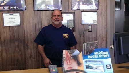 Man in blue shirt at a counter, inside an auto shop. Wooden paneling in the background, pamphlets visible.