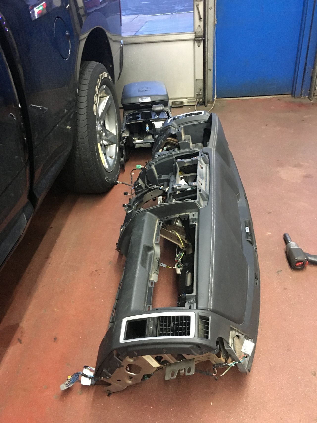 Car dashboard removed in a garage, with tools and car parts visible.