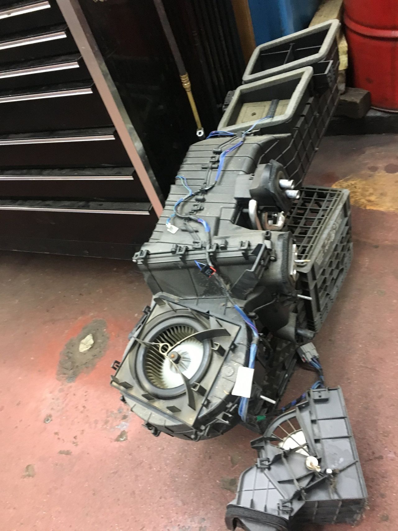 Car's air conditioning unit disassembled on a shop floor; components include vents, fan, and ducting.