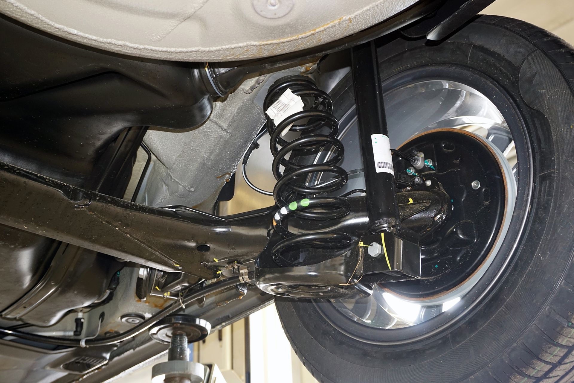Undercarriage of a car, showing rear suspension, black components, tire, and shock absorber.