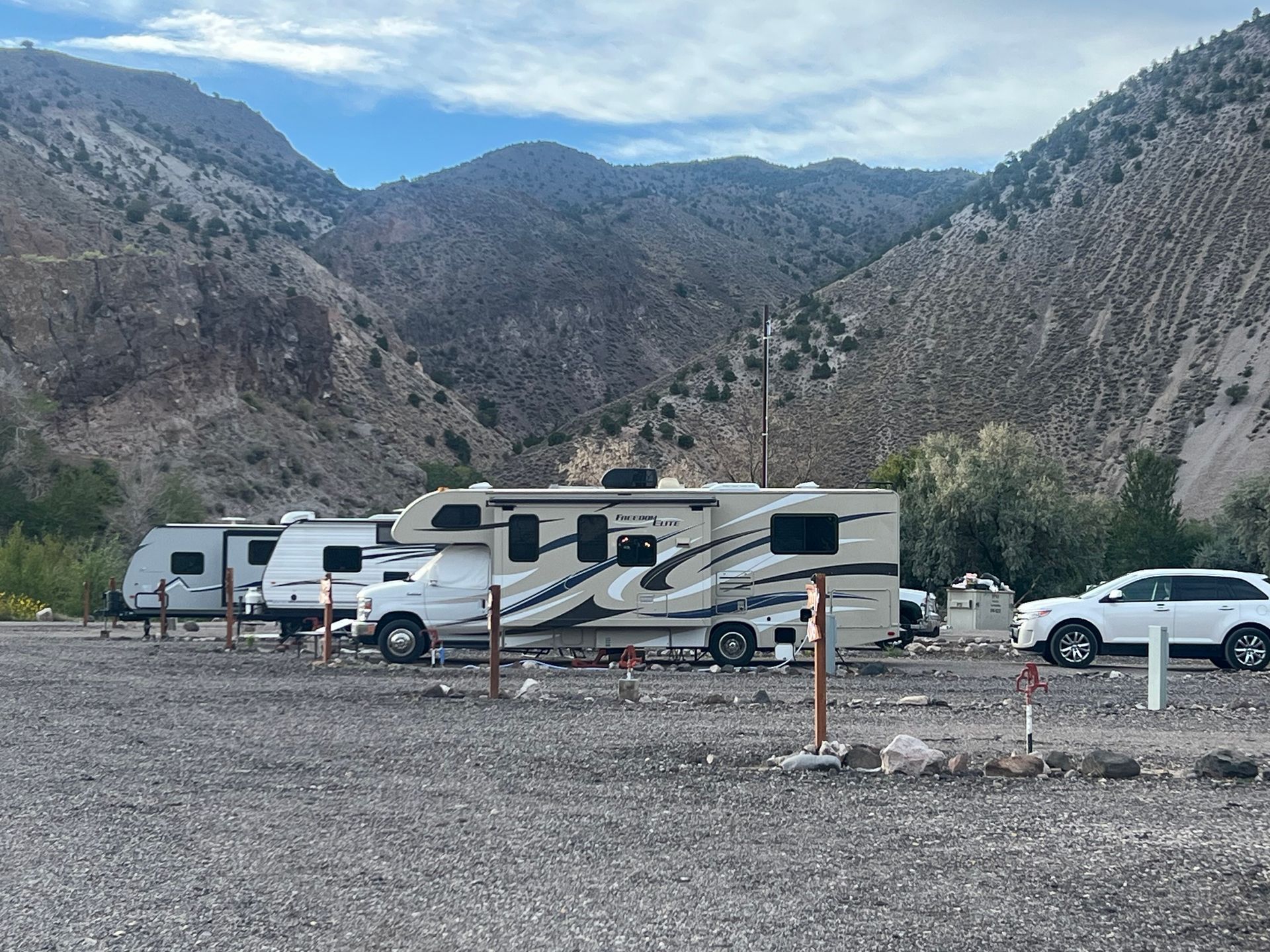 RVs parked in a gravel lot with mountains in the background. Cloudy day.