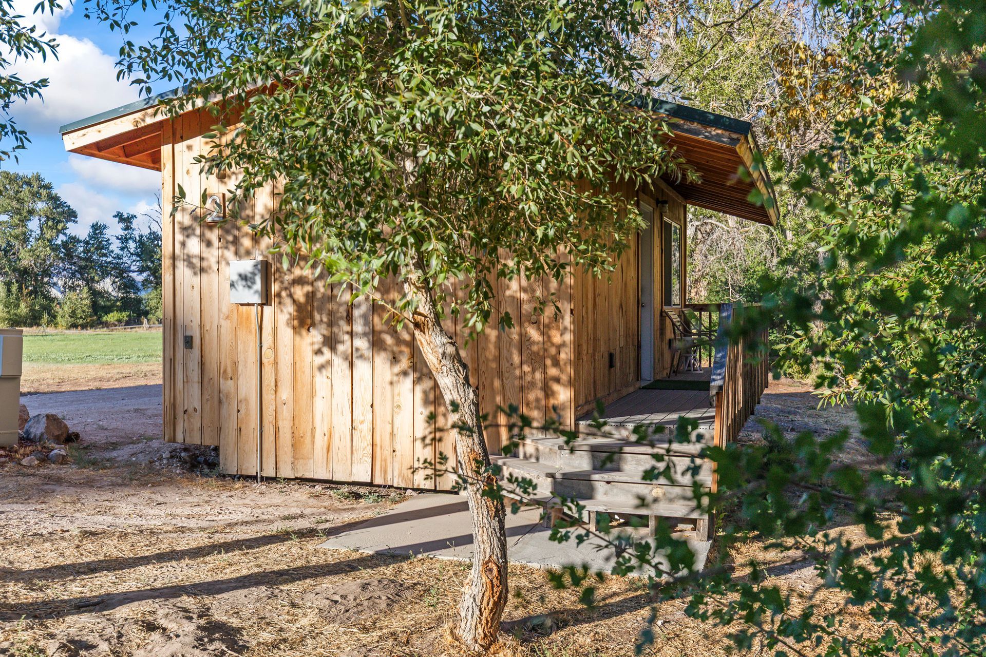 Wooden cabin with small porch and steps, surrounded by trees and a field.