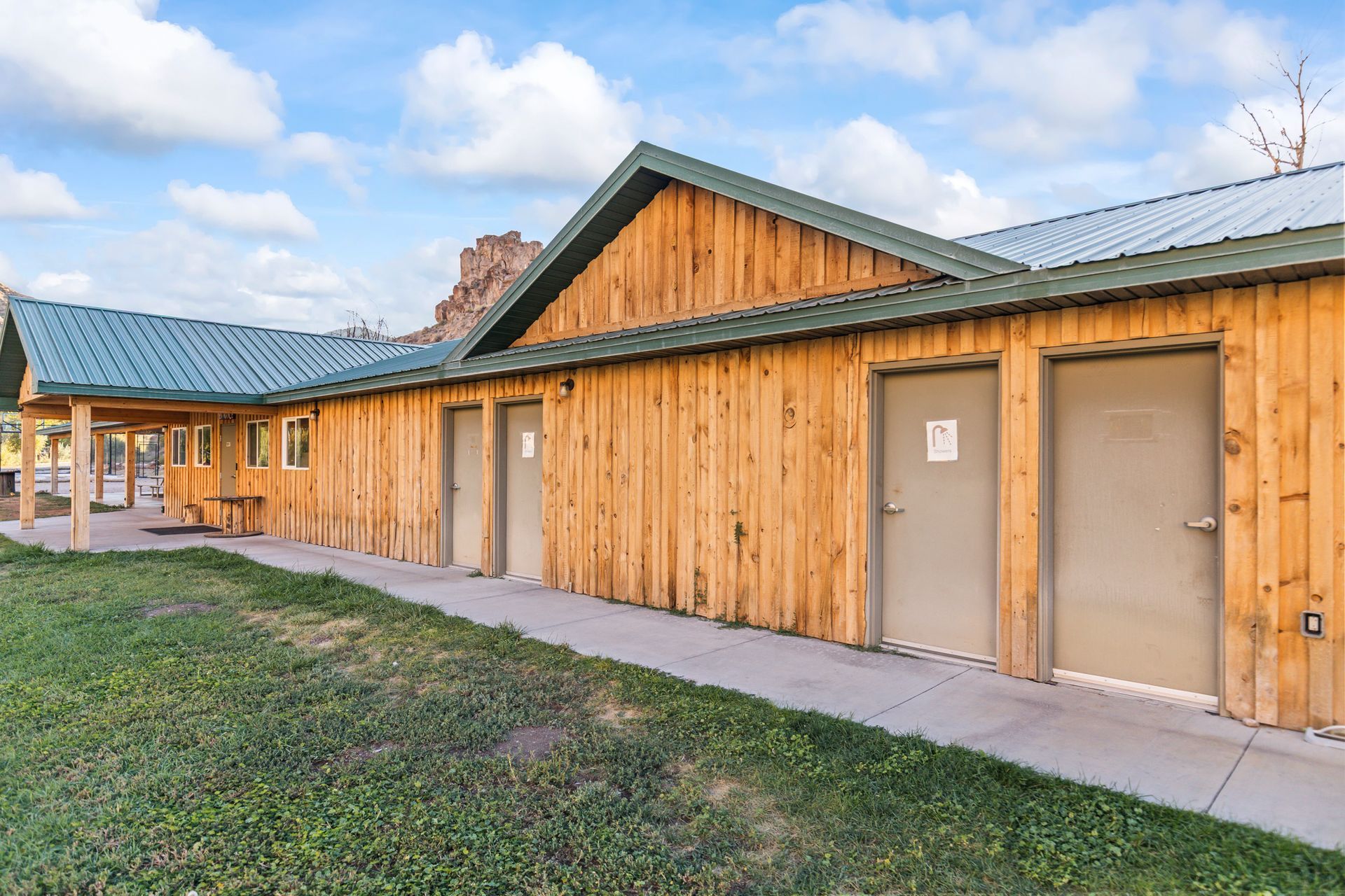 Wooden building with multiple bathroom doors under a green roof; exterior shot.
