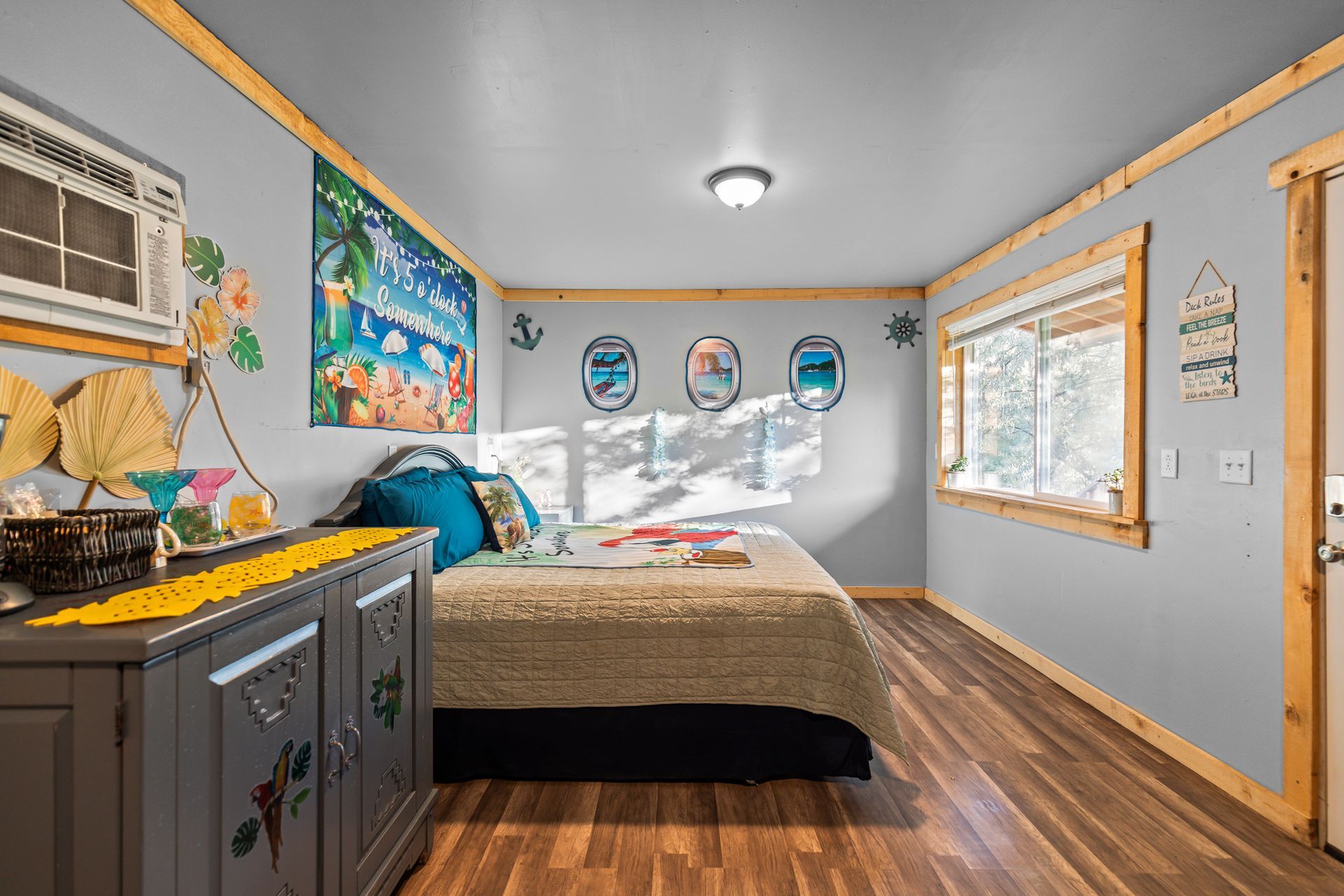 Small bedroom with bed, dresser, and window, blue walls, wood trim.