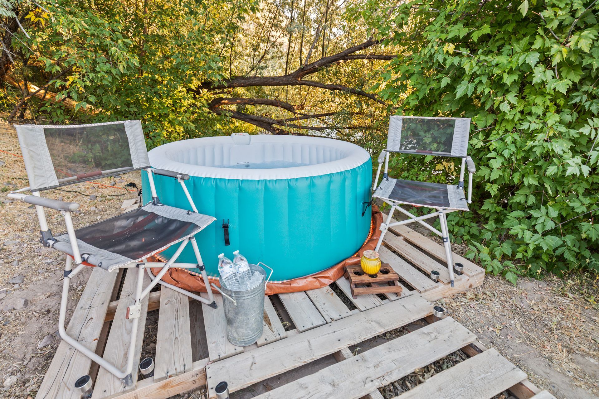 Turquoise inflatable hot tub on wooden pallets with two folding chairs, drinks, and lemon. Outdoors.