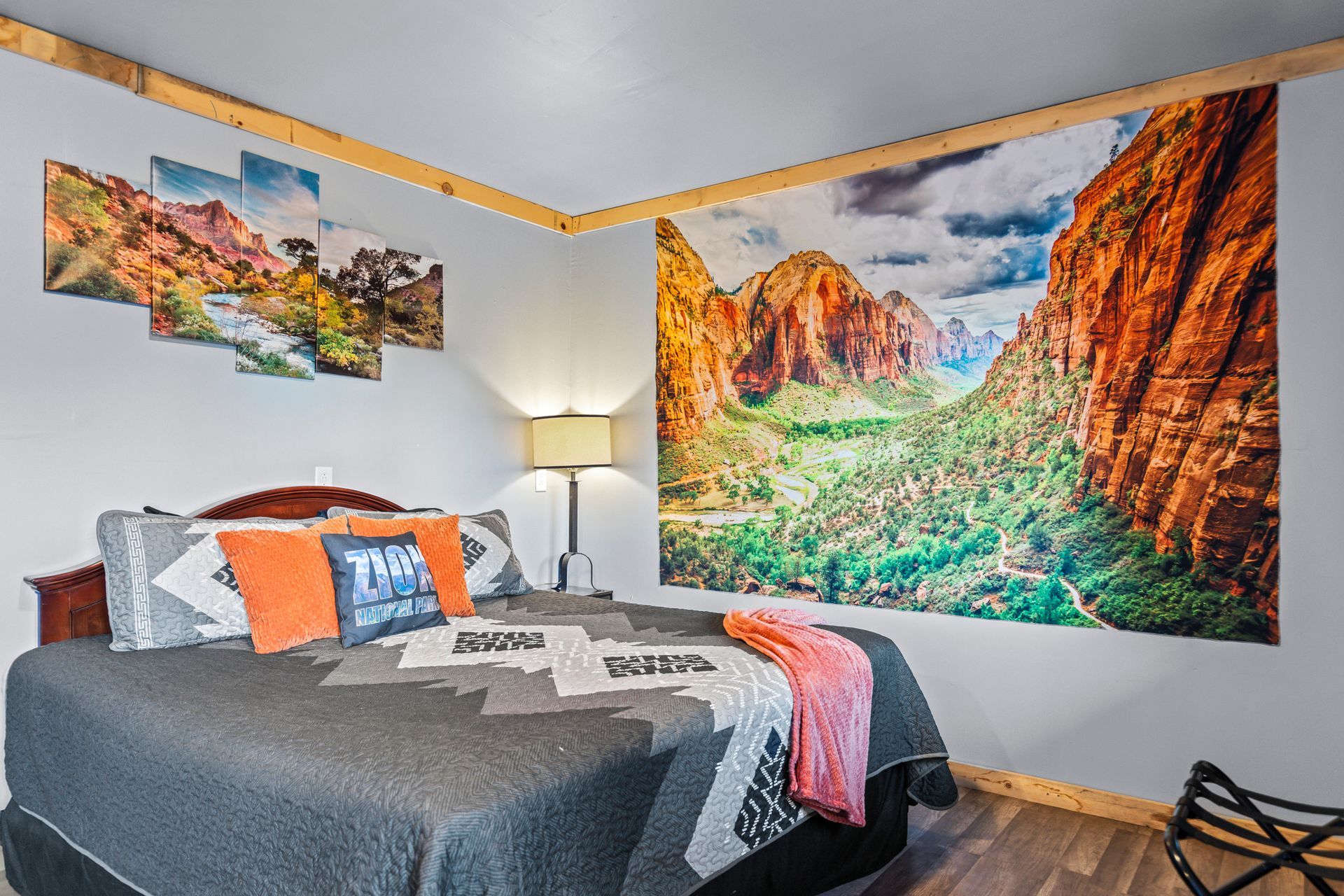 Bedroom with large mountain landscape art and a bed with decorative pillows and a blanket.