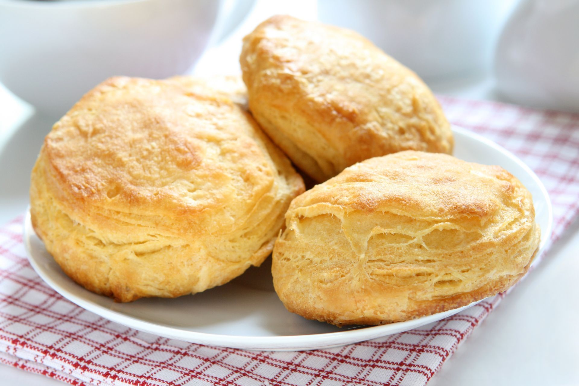 Fluffy golden biscuits on a white plate, set on a red and white checkered cloth.