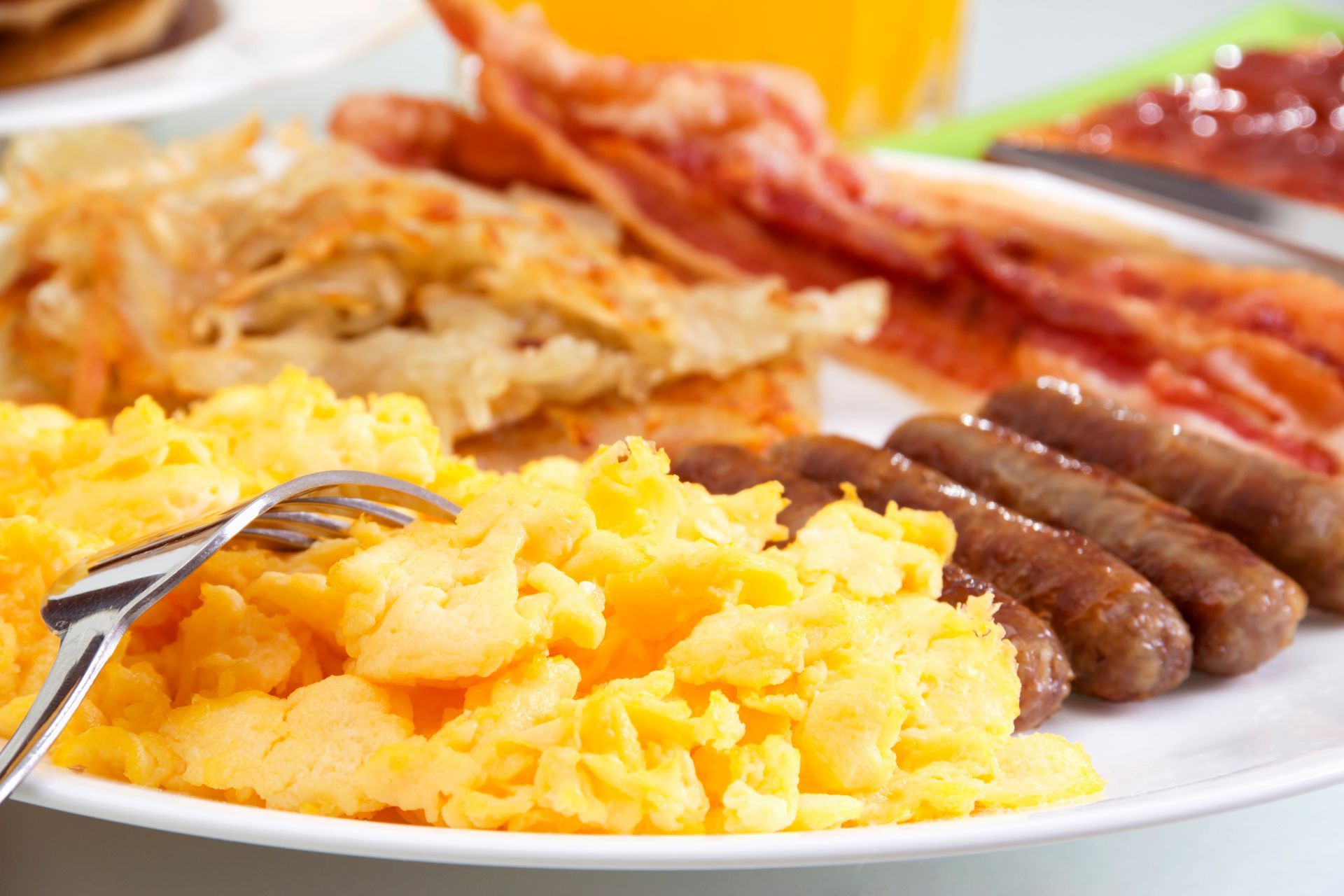 Plate of breakfast food: scrambled eggs, bacon, sausage, hash browns.