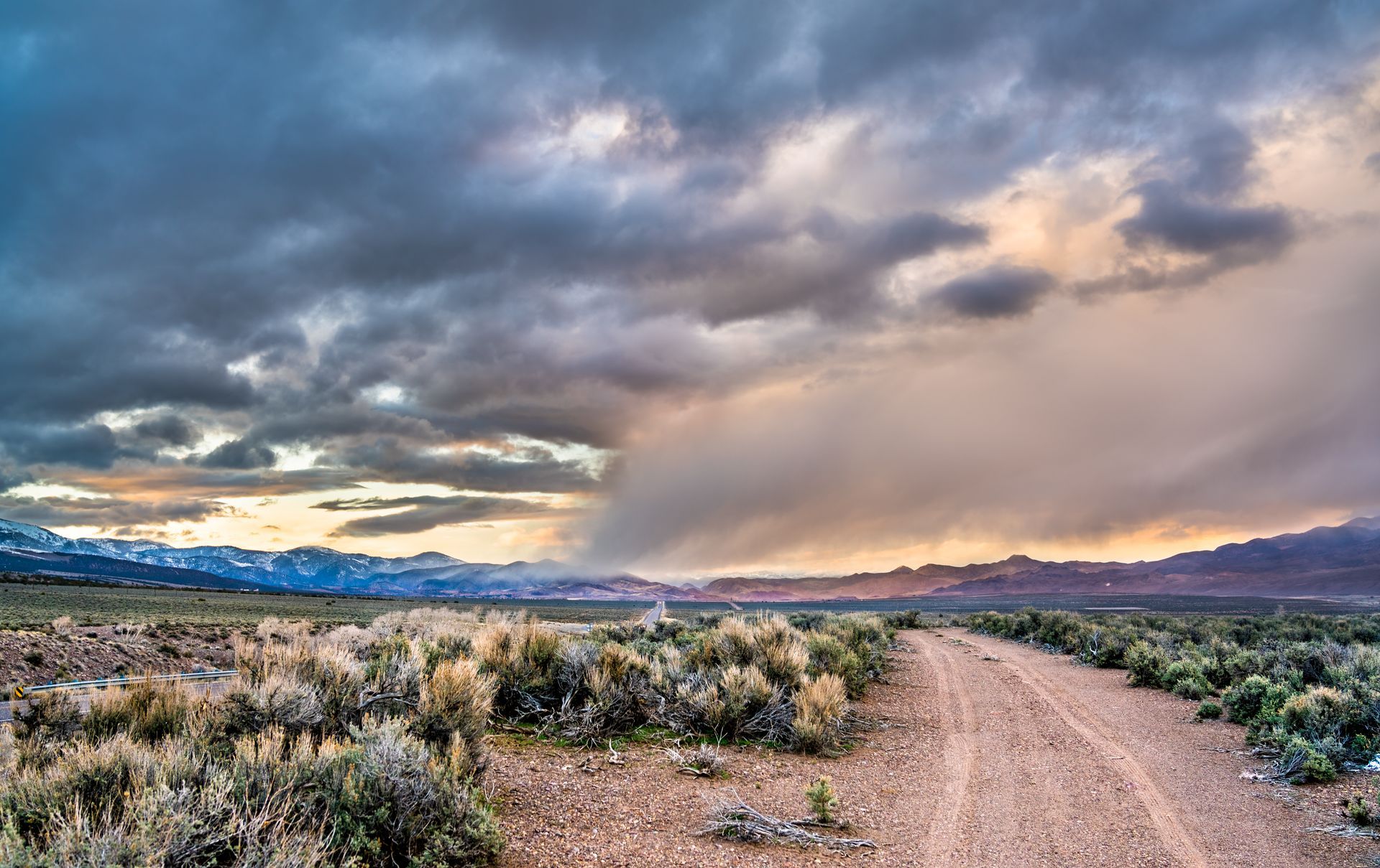 A dirt road in the desert with a cloudy sky in the background.