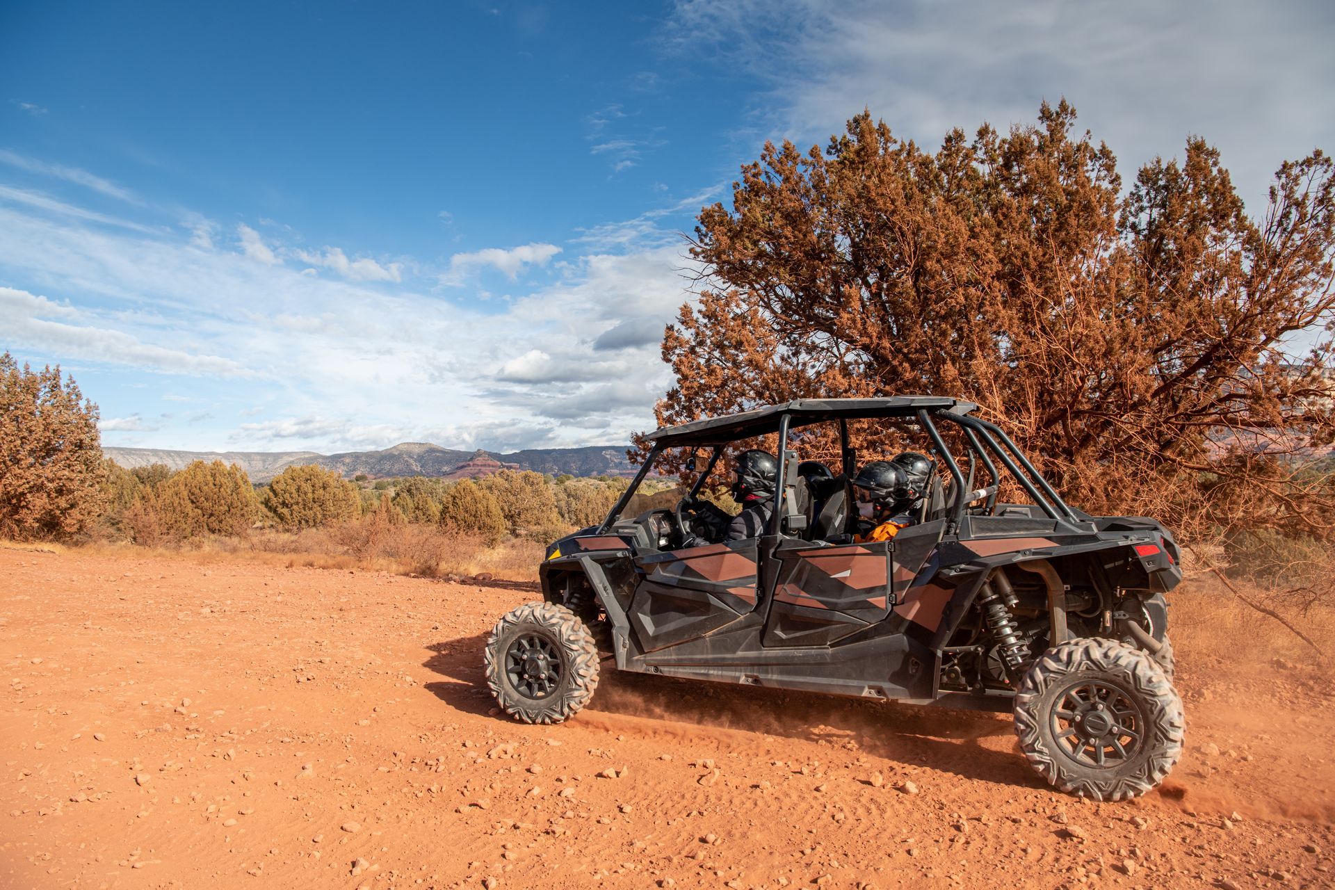 ATV with passengers on a red dirt road in a desert landscape.