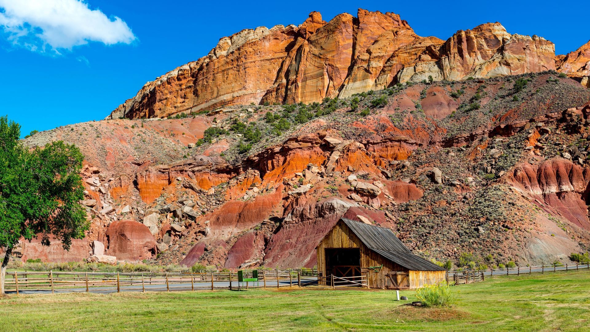 There is a barn in the middle of a grassy field with a mountain in the background.