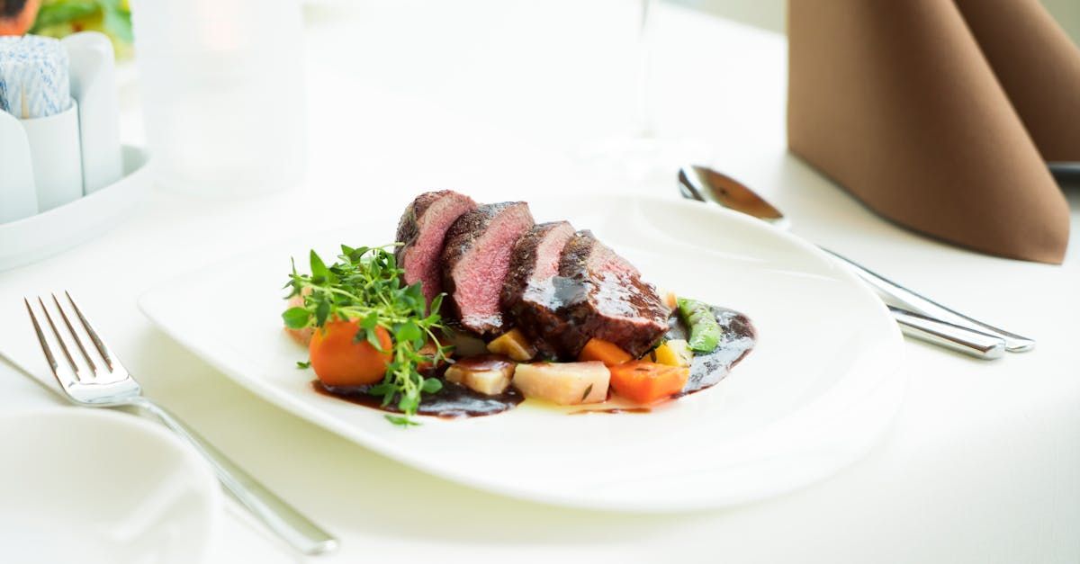 A white plate topped with a piece of meat and vegetables on a table.