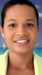 Woman with brown skin smiling, wearing a yellow blazer and silver earrings; beach background.