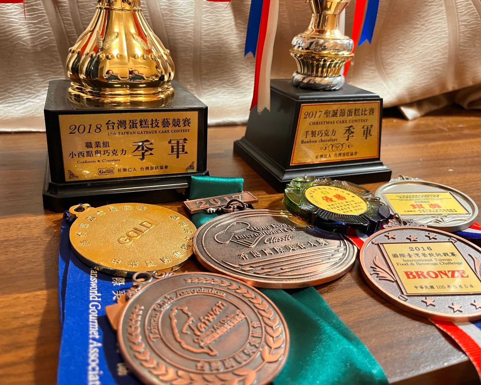 獎盃和獎牌擺放在一個平面上。獎盃是金色和黑色的，獎牌是銅色、金色和銀色的。