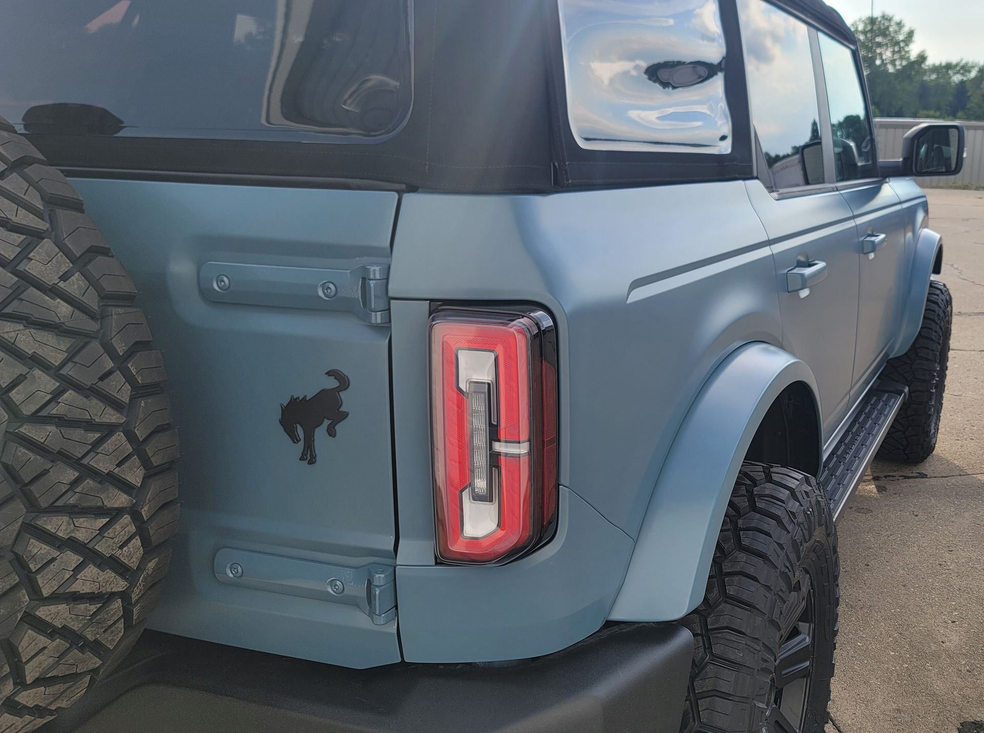 Blue Ford Bronco SUV with black soft top, large tires, and black horse silhouette on the back.