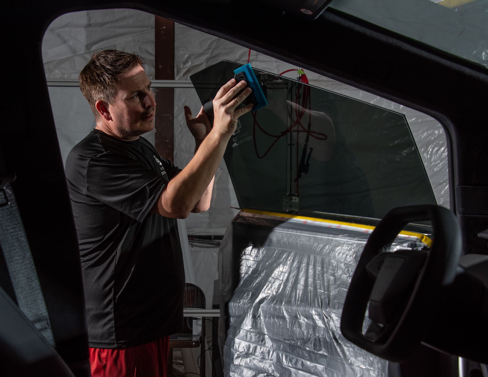 A man with a tattoo on his arm is cleaning the windshield of a car.