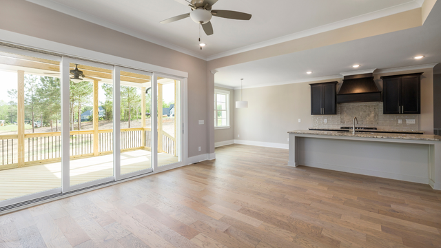 Open-concept living space with wood floors, sliding glass doors to a porch, and a kitchen with dark cabinets.