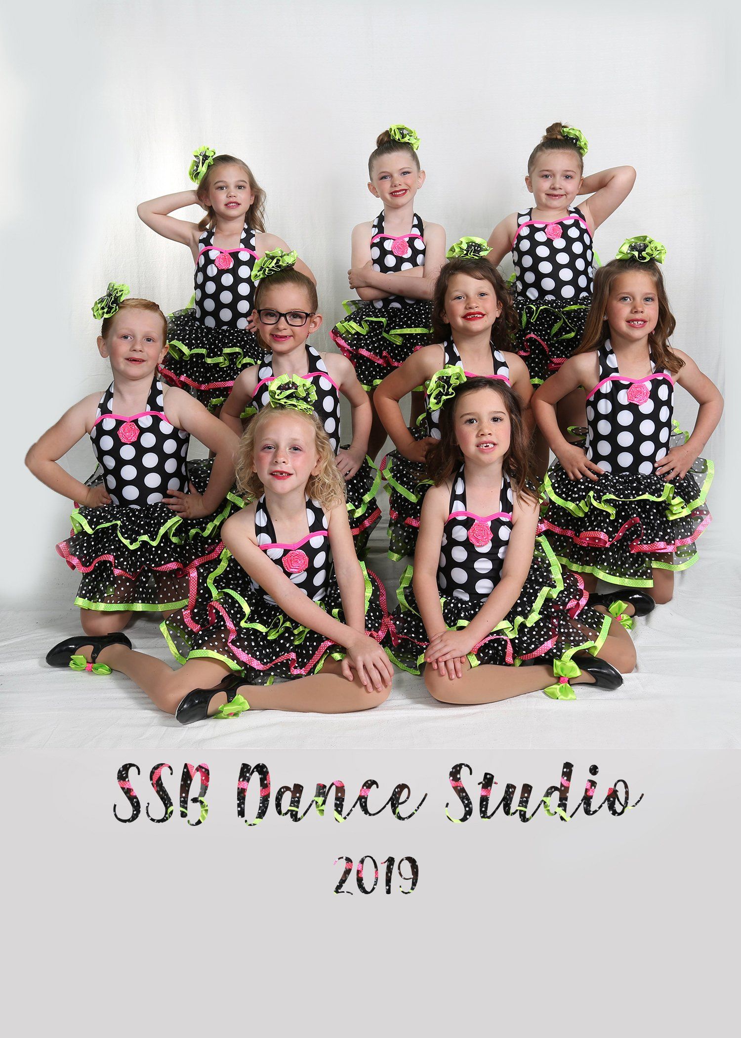 Group of young girls in polka-dot dresses and neon tutus posing for a dance studio photo.