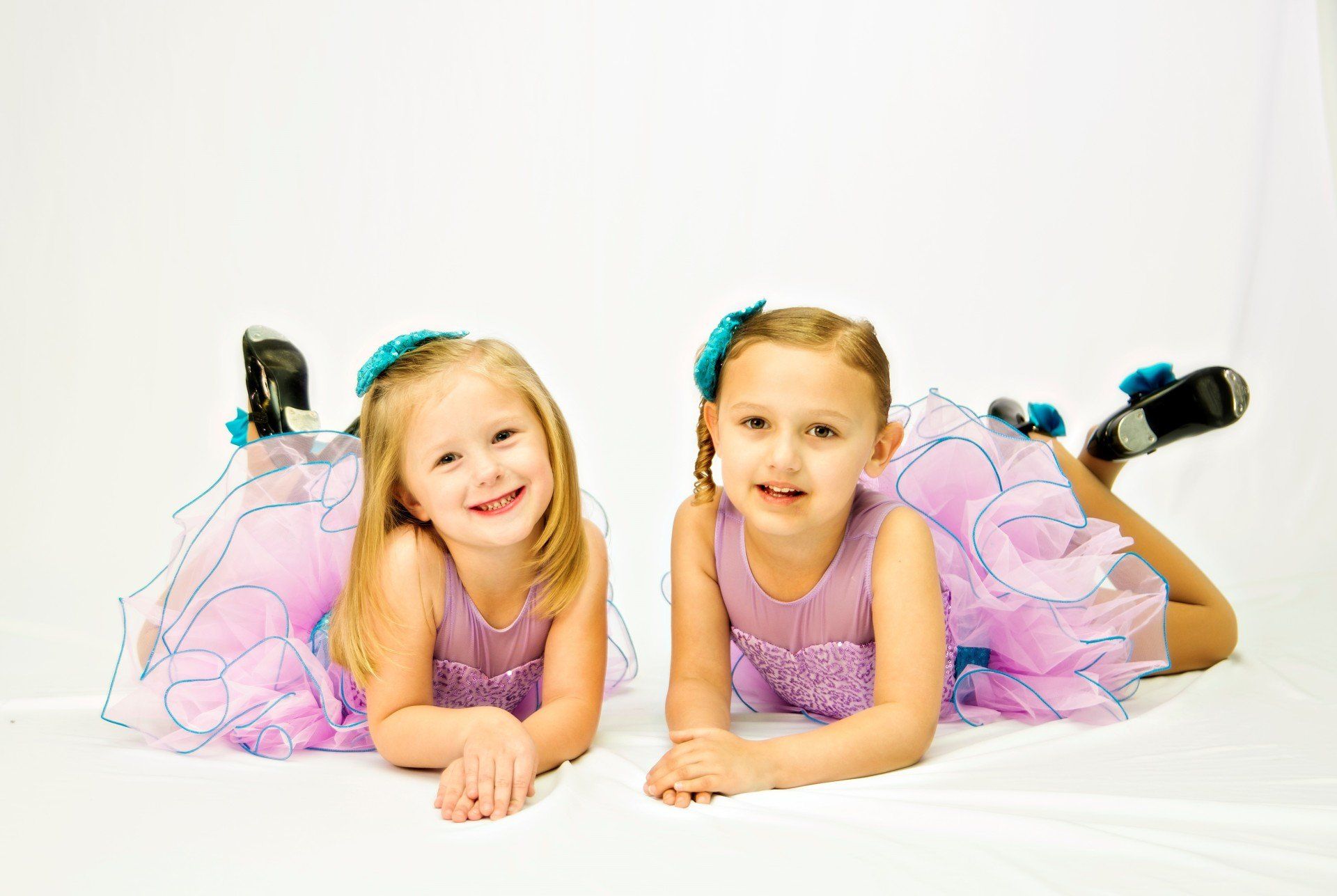 Two young girls in dance costumes smiling, lying on the floor.