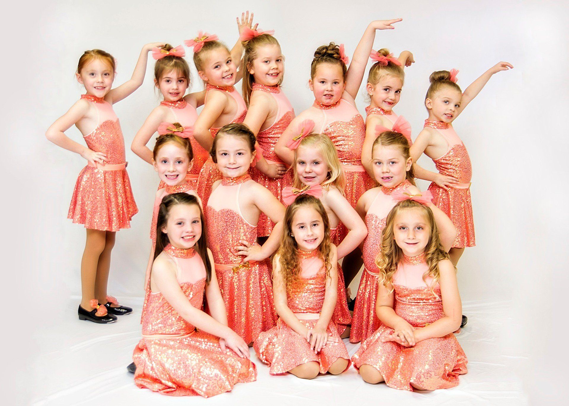 A group of young girls in coral sequined dresses smiling, posing together.
