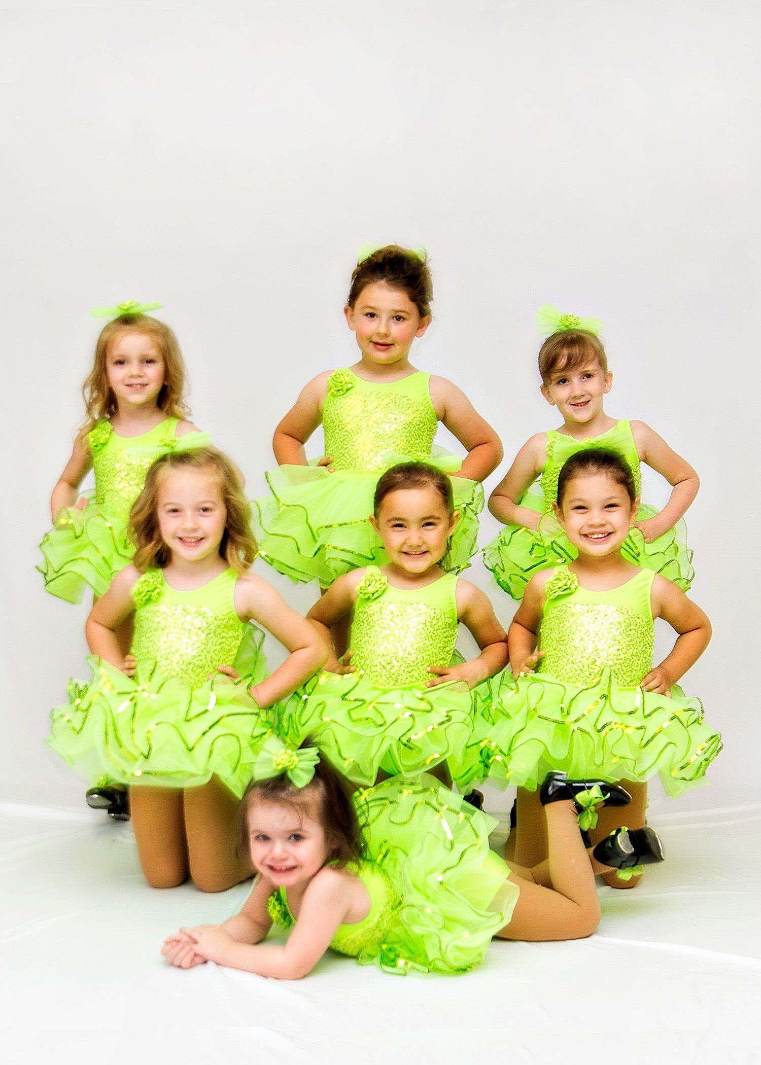 Seven young dancers in lime green costumes pose in a studio.