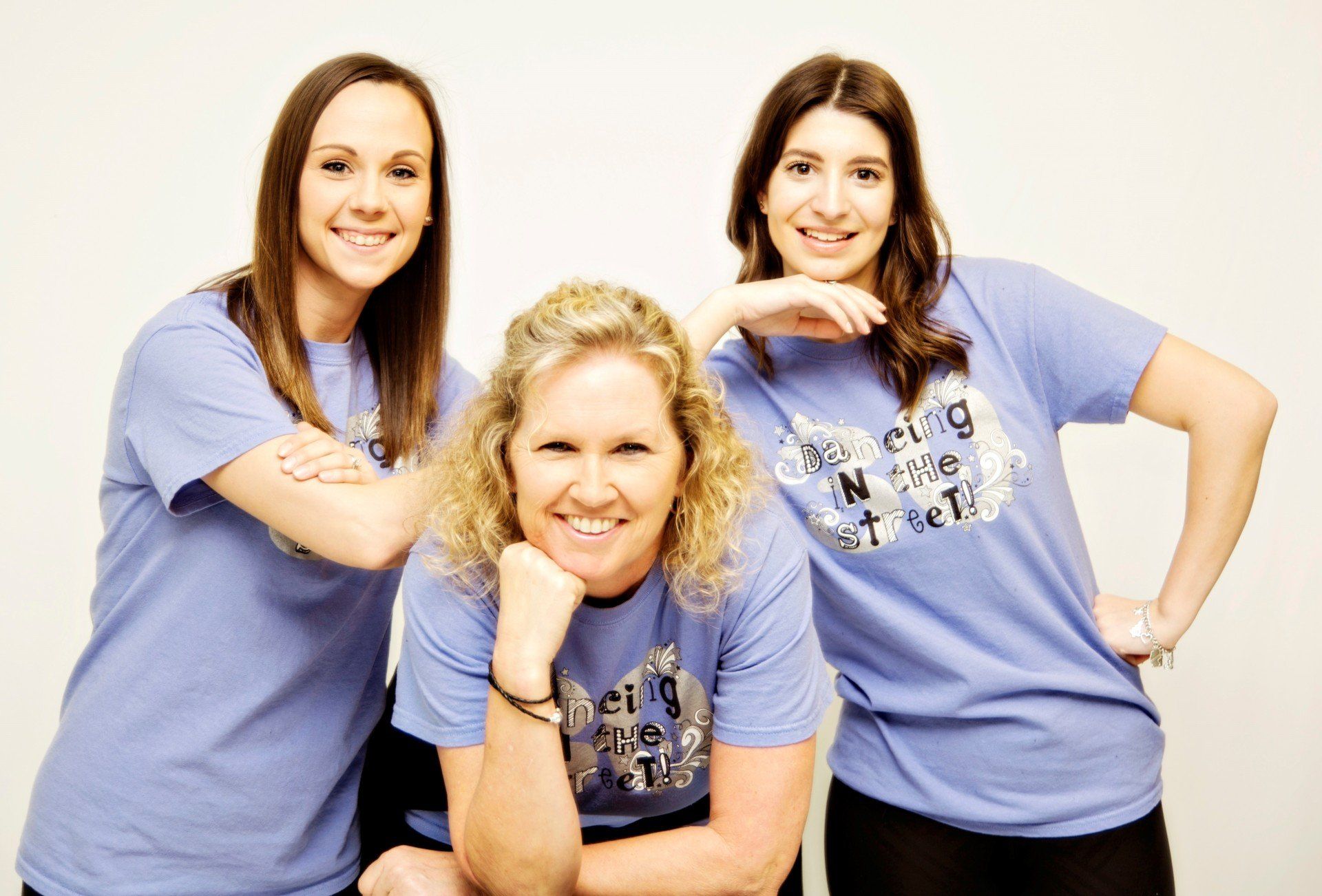 Three women in light blue shirts pose, smiling, against a white background.