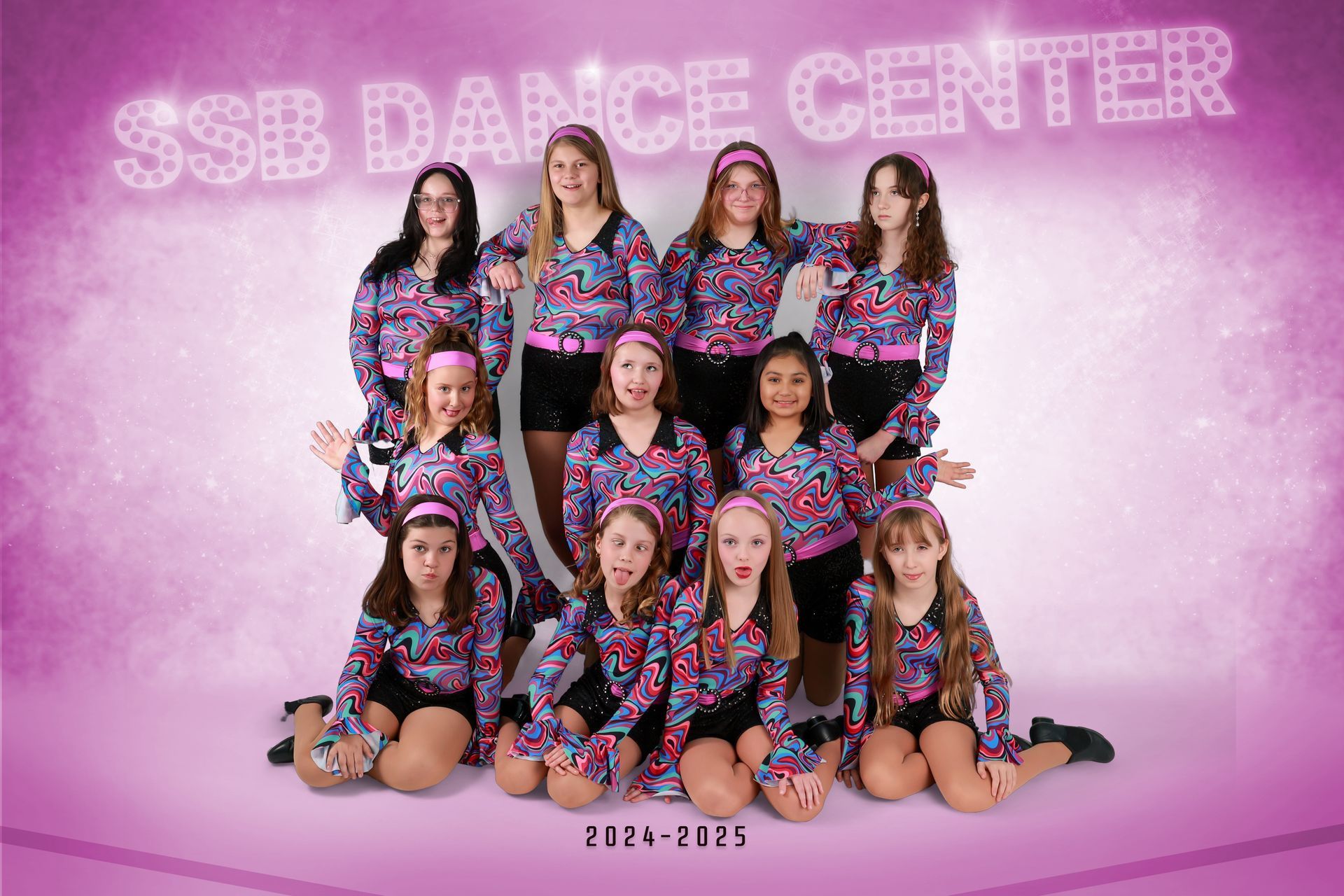 SSB Dance Center group photo. 11 girls in patterned tops, black shorts, pink background. 2024-2025.